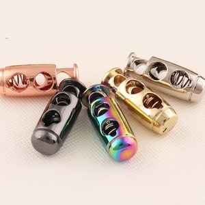 May include: Five different colored cord stoppers with a spring mechanism. The stoppers are made of metal and have a cylindrical shape. The colors are rose gold, black, gold, silver, and iridescent.