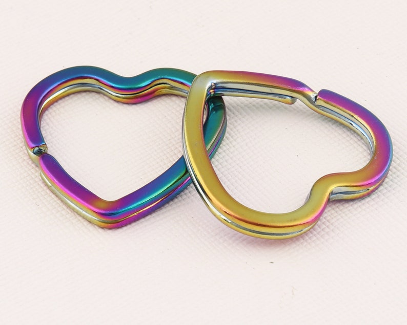 K&ouml;nnte beinhalten: Zwei regenbogenfarbene herzf&ouml;rmige Schl&uuml;sselanh&auml;nger mit silberner Oberfl&auml;che. Die Schl&uuml;sselanh&auml;nger sind miteinander verbunden.