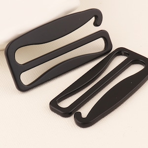 May include: Three black metal bra strap adjusters. The adjusters have a hook on one end and a loop on the other end.