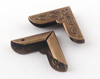 May include: Two antique brass corner protectors with an ornate design. The protectors are made of metal and have a vintage look.