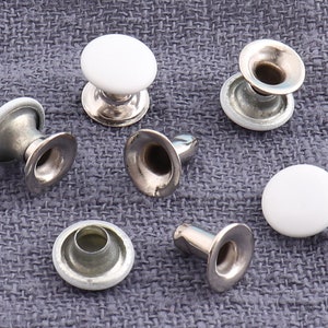 Puede incluir: Surtido de botones a presión de metal blanco y plateado. Los botones a presión se utilizan para unir tela o cuero.