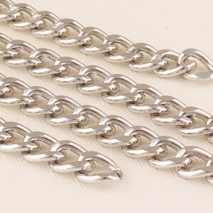 May include: Close-up of three silver curb chains with a flat, rectangular link design. The chains are arranged in a staggered pattern, with the ends of the chains visible.
