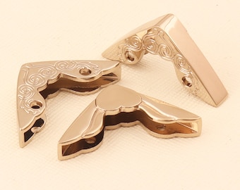Può includere: Tre proteggi angoli in metallo color oro con un designo decorativo a spirale. I proteggi angoli sono progettati per proteggere gli angoli di mobili o altri oggetti.