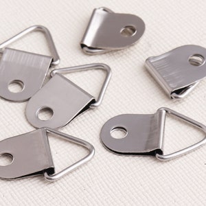 May include: Six silver-toned metal picture hanging hooks with a triangular shape. The hooks have a small hole in the center of the triangle.