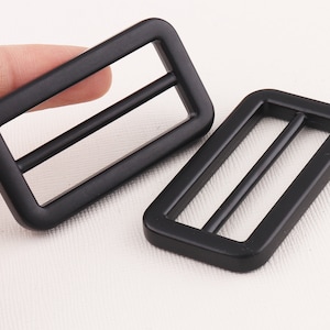 May include: Two black plastic slider buckles. The buckles are rectangular with a smooth, matte finish.
