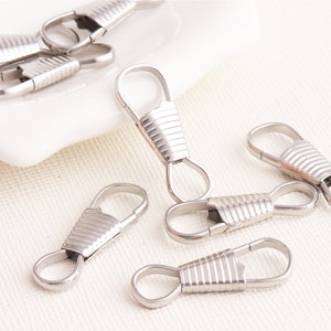 Pode incluir: Clipes de chaveiro de metal prateado com um design texturizado. Os clipes têm um laço em uma extremidade e um fecho de mola na outra extremidade.