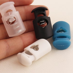 Puede incluir: Cuatro cierres de cordón de plástico en diferentes colores: transparente, negro, blanco y azul. Cada cierre de cordón tiene un resorte en el interior y un agujero para que pase un cordón.