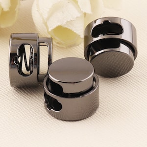 May include: Three black metal cord stoppers with a spring mechanism. The stoppers are round and have a smooth finish.