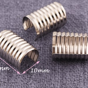 Puede incluir: Tres anillos de metal plateado con textura acanalada. Los anillos miden 14 mm de largo y 10 mm de ancho.