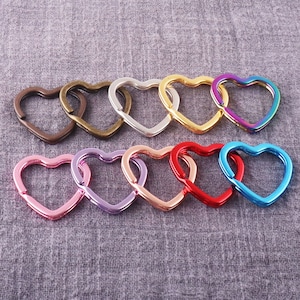 May include: Assortment of ten heart-shaped metal key rings in various colors, including silver, gold, pink, purple, red, and blue.