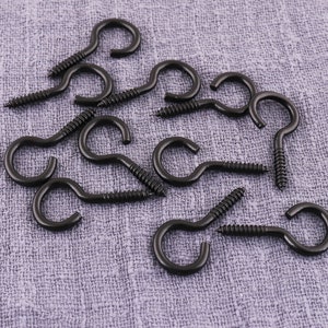 May include: A close-up of a group of black metal screw-in hooks with a rounded loop at the end. The hooks are scattered on a gray fabric surface.