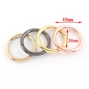 Puede incluir: Tres llaveros de metal en dorado, negro y oro rosa. El llavero de oro rosa mide 49 mm de ancho y 38 mm de diámetro.