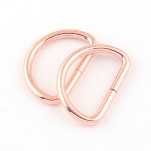 May include: Two rose gold metal D-rings. The rings are smooth and shiny.