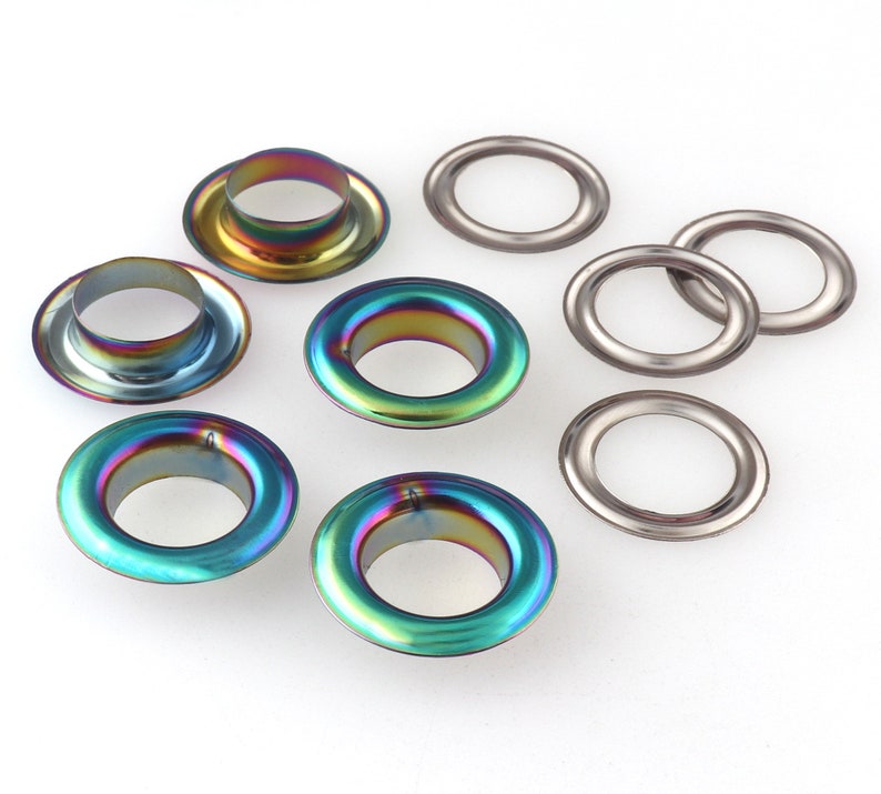 Op de afbeelding: Assortiment van metalen oogjes in zilver en regenboogkleuren. De oogjes zijn in verschillende maten en zijn ideaal voor knutselprojecten.