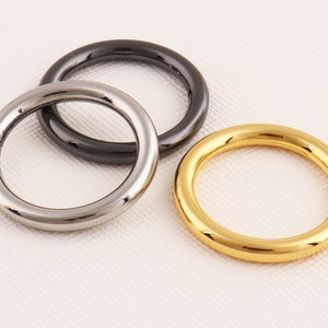 May include: Three metal rings, one silver, one gold, and one black.