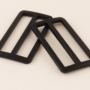 May include: Two black plastic slider buckles. The buckles are rectangular with two parallel slots in the center.