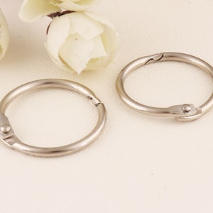 May include: Two silver metal binder rings. The rings are open and ready to be used to bind papers together.