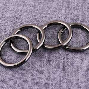 May include: Four black metal rings of different sizes, stacked on top of each other. The rings are smooth and shiny.