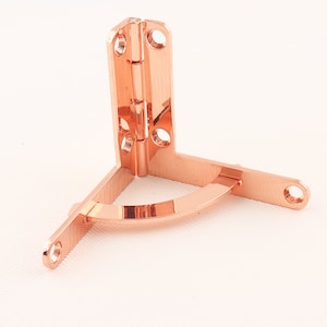 Könnte beinhalten: Ein Eckband aus Roségold mit abgerundeter Kante. Das Band ist aus Metall und hat eine polierte Oberfläche.