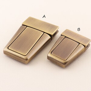 May include: Two antique gold-toned metal clasps, labelled A and B, for attaching straps or bags. The clasps are rectangular with a raised, rectangular centre section.