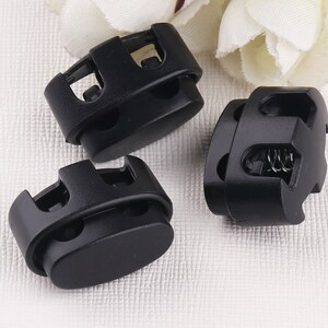 Puede incluir: Tres cierres de cordón de plástico negro con un mecanismo de resorte. Los cierres de cordón están diseñados para asegurar cordones o correas.