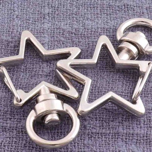 Puede incluir: Llavero de metal plateado con dos clips giratorios en forma de estrella y un anillo redondo.