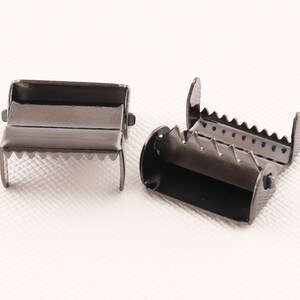 May include: Two black metal slider buckles with teeth on the edges. The buckles are designed to be used with webbing or straps.