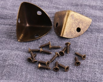 May include: Two antique gold corner brackets with a set of 12 screws. The brackets are triangular and have a distressed finish. The screws are small and have a star-shaped head.