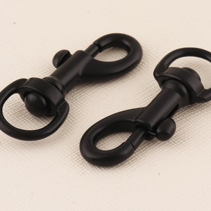 Puede incluir: Dos mosquetones giratorios de metal negro. Los mosquetones tienen una puerta con resorte y un bucle giratorio.