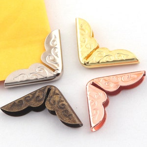 Puede incluir: Cuatro protectores de esquina decorativos con un diseño de espiral. Los protectores están hechos de metal y vienen en oro, plata, bronce y oro rosa.