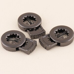 May include: Three black metal clasps with a spring mechanism. The clasps are designed to be used for attaching clothing or other items.