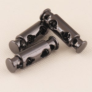 May include: Three black metal cord stoppers with a spring mechanism. Each stopper has a heart-shaped design.