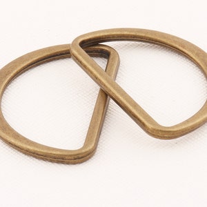 May include: Two antique gold-toned metal D-rings, one slightly larger than the other, are interlocked. The rings are smooth and have a slightly rounded edge.