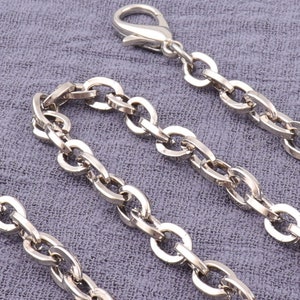 May include: A silver chain with a lobster clasp. The chain is made of oval links.