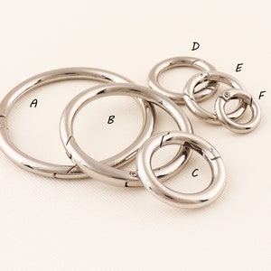 Könnte beinhalten: Sechs silberne Schlüsselringe aus Metall in verschiedenen Größen. Die Ringe sind mit A bis F beschriftet.