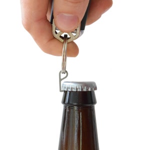 May include: A silver bottle opener attached to a keychain is being used to open a brown glass bottle.