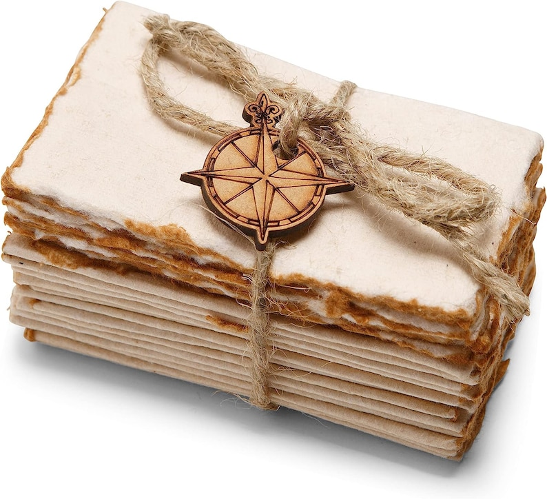 K&ouml;nnte beinhalten: Ein Stapel handgemachtes Papier, gebunden mit Schnur und einem Holz-Kompass-Anh&auml;nger. Das Papier hat ein nat&uuml;rliches, rustikales Aussehen und Gef&uuml;hl.