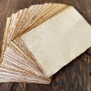 K&ouml;nnte beinhalten: Ein Stapel handgemachtes Papier in nat&uuml;rlichen Braun- und Wei&szlig;t&ouml;nen. Das Papier ist aus recycelten Materialien hergestellt und hat eine raue Textur.