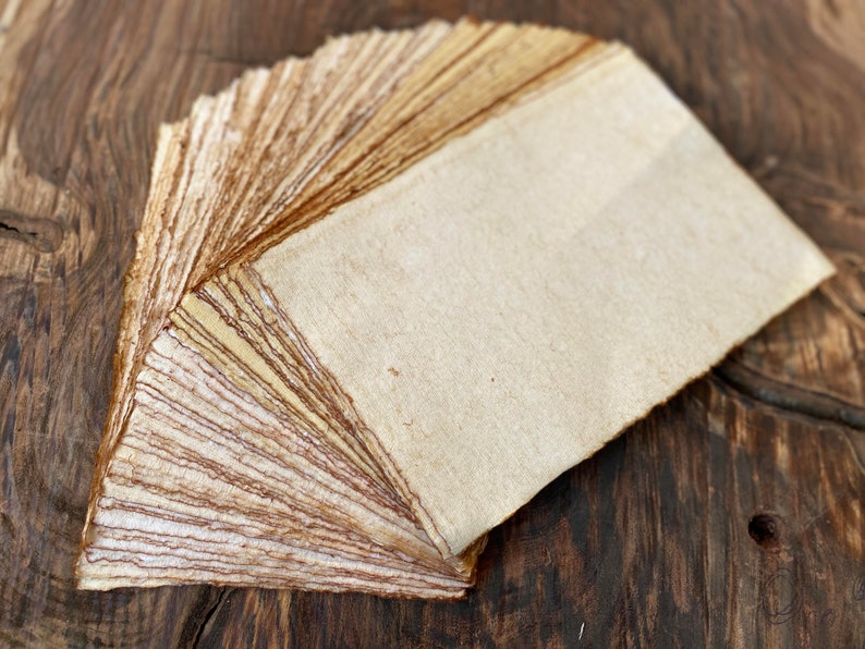K&ouml;nnte beinhalten: Ein Stapel handgemachtes Papier in nat&uuml;rlichen Braun- und Wei&szlig;t&ouml;nen. Das Papier ist aus recycelten Materialien hergestellt und hat eine raue Textur.