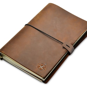 May include: A brown leather journal with a compass rose emblem. The journal is closed with a black elastic band and a leather strap. The pages are cream-colored, and the journal has a vintage aesthetic.