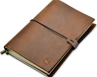 Könnte beinhalten: Ein braunes Lederjournal mit einem Kompassrosen-Emblem. Das Journal wird mit einem schwarzen Gummiband und einem Lederriemen verschlossen. Die Seiten sind cremefarben und das Journal hat eine Vintage-Ästhetik.