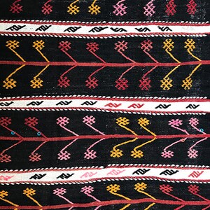 May include: Black and white woven fabric with a repeating geometric pattern in red, pink, and yellow. The pattern features small flowers and zig-zag lines.