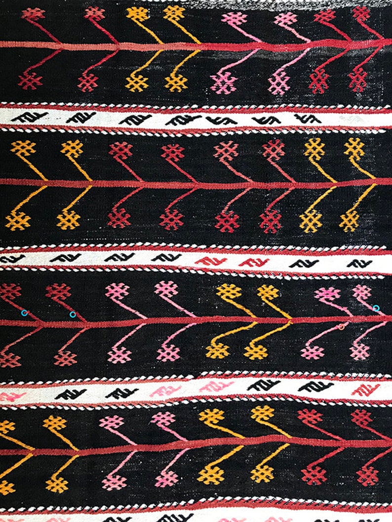 May include: Black and white woven fabric with a repeating geometric pattern in red, pink, and yellow. The pattern features small flowers and zig-zag lines.