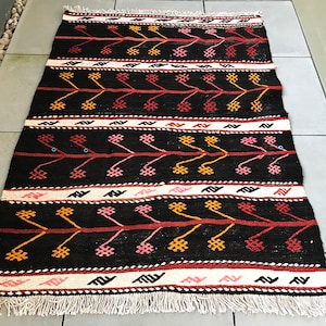 May include: A black and white rug with a geometric pattern in red, orange, and pink. The rug has a fringe border.