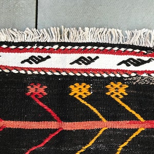 May include: Close-up of a black and white rug with red, yellow and pink geometric patterns. The rug has a white fringe border.