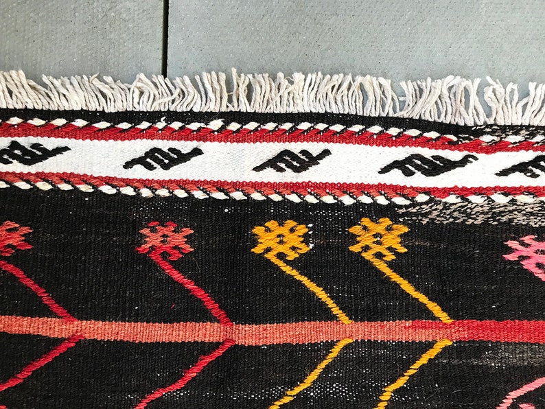 May include: Close-up of a black and white rug with red, yellow and pink geometric patterns. The rug has a white fringe border.