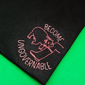 Könnte beinhalten: Schwarzes T-Shirt mit rosa gesticktem Text "Become Ungovernable" und einem Comic-Bären.