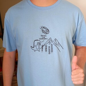 May include: A light blue t-shirt with a black graphic of a dinosaur looking up at a falling comet with the text "Oh no, the economy!"