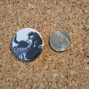 Puede incluir: Un botón en blanco y negro con una imagen de primer plano de un hombre con barba mirando hacia arriba.