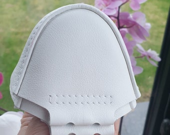 May include: White leather face mask with a stitched seam across the front. The mask is folded in half and held in a hand.